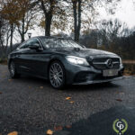 En elegant Mercedes C300 Coupe parkeret på en asfaltvej omgivet af efterårsblade under en humørfyldt, overskyet himmel, der viser luksus og elegance.
