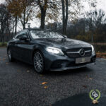 En slank sort Mercedes C300 Coupe parkeret på en våd asfaltvej, prydet med nedfaldne blade, på en overskyet efterårsdag.