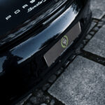 Et vinklet nærbillede af en elegant sort Porsche Boxster S, der fremhæver dens ikoniske badge og modelnavn, med en europæisk nummerplade, sat mod en brostensbelagt gade.