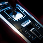 Et nærbillede af en luksus Boxster S-bils automatgearstang omgivet af avancerede betjeningselementer og rødt læderbetræk, der viser bilens sporty, men elegante interiørdesign.