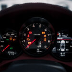 Et oplyst Boxster S bilinstrumentbræt om natten, der viser forskellige advarselslys, et omdrejningstæller, et speedometer og et informationsdisplay, der angiver, at bilen holder stille og udetemperaturen er 16 grader