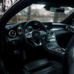 Et førerperspektiv ind i den moderne kabine i en Mercedes C300 Coupe, med et læderbeklædt rat med betjeningselementer, indviklet instrumentbræt og raffineret midterkonsol, alt omsluttet af høj kvalitet