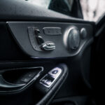 Et interiørbillede af luksusbiler, specifikt Mercedes C300 Coupes førersidedør, med fokus på metal- og læderdetaljerne på kontrolpanelet, med regndråber synlige på vinduet.
