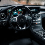 Et elegant Mercedes C300 Coupe interiør viser et luksuriøst instrumentbræt med oplyste målere bag et læderrat, sammen med avanceret trim og betjeningselementer, set fra førersædets perspektiv med en regnpletter