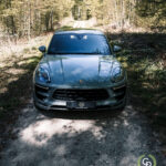 En elegant sølvfarvet Porsche Macan GTS på en grusvej midt i en fredfyldt skov, der afspejler skønheden i dens naturlige omgivelser.
