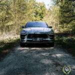 En luksus-SUV, nærmere bestemt en Porsche Macan GTS, parkeret på en grussti, omgivet af frodige grønne træer, der soler sig i sollys og udstråler en følelse af ydeevne og elegance.