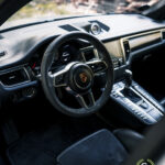 Indvendigt billede af et Porsche Macan GTS-køretøj, der fremhæver rattet med logoet, midterkonsollen og luksuriøse detaljer.