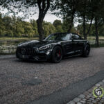 En slank sort Mercedes-Amg Gt C roadster parkeret ved en fredfyldt søbred, der viser sit sporty design og luksuriøse attitude midt i en kulisse af frodige grønne områder.