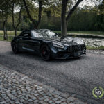 En slank sort Mercedes-Amg Gt C roadster parkeret ved siden af en rolig sø, der emmer af luksus og ydeevne med sin aggressive stil under skumringens bløde skær.