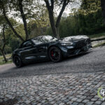 En slank sort Mercedes AMG GT C Roadster parkeret på en brostensbelagt sti, der viser sit dynamiske design og sportsvognstiltrækning midt i rolige parkomgivelser.