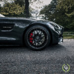 Et nærbillede af en sort Mercedes AMG GT Roadster V8 biturbo, med fokus på dens blanke maling, stilfulde alufælge med karakteristiske bremsekaliber, optaget på en rolig baggrund af