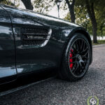 En sort luksus-roadster fremviser sit V8 biturbo-emblem, slanke karrosseri, højtydende bremser med røde kaliber og førsteklasses multi-eger alufælge, parkeret ved en gade med træer.