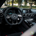 Et luksuriøst bilinteriør med et Mercedes AMG GT C-rat med monterede kontroller, et digitalt instrumentbræt, centralkonsol med infotainmentsystem og førsteklasses finish.