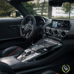 Luksuriøst Mercedes AMG GT C interiør med et moderne instrumentbræt med touchscreen infotainmentsystem, lædersæder med røde syninger og en slank midterkonsol med metalliske accenter, der viser sofistikeret design og avanceret teknologi