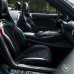 Et elegant interiørbillede af den højtydende Mercedes AMG GT C Roadster, med luksuriøse lædersæder med røde detaljer, et sofistikeret instrumentbræt og det karakteristiske AMG-emblem, der symboliserer en sammensmeltning af