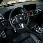 Indvendigt billede af en BMW X3 xDrive30e hybrid SUV, der viser rattet med logo, digitalt instrumentbræt, infotainmentsystem og luksuriøse sorte lædersæder med fokus på moderne design og