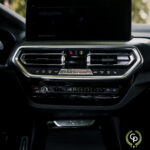 En moderne BMW X3 xDrive30e hybrid SUV's slanke instrumentbræt med et touchscreen display med en "velkommen"-besked, klimakontroller og et minimalistisk sort interiør med metalliske accenter, der viser avanceret