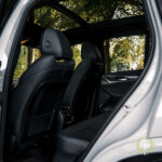 En visning af BMW X3 xDrive30e Plug-in Hybrid's interiør gennem en åben dør, der fremhæver de slanke sorte lædersæder og det elegante design af instrumentbrættet med en grøn baggrund
