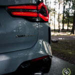 Et nærbillede af en BMW X3 xDrive30e, der fremhæver dens skulpturelle bagdesign, karakteristiske LED-baglygter og sportslige dobbelte udstødningsspidser, parkeret midt i en fredfyldt skovkulisse