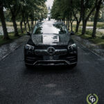 En elegant, luksuriøs SUV, Mercedes GLE350de plug-in hybrid parkerer på en træbeklædt indkørsel, dens front vender mod kameraet og viser en regndråbeplettet motorhjelm og det ikoniske emblem