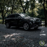 En elegant sort Mercedes GLE350de SUV parkeret på en brostensbelagt sti i skyggen af frodige grønne træer, der viser luksus og moderne hybriddesign.