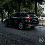 En elegant sort hybrid SUV parkeret på en brostensbelagt gade, flankeret af træer, fremviser blank lak under en overskyet himmel med emblemet for sit luksusmærke, Mercedes GLE350