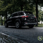 En elegant sort Mercedes GLE350de hybrid SUV parkeret på en brostensbelagt gade, der viser sit dynamiske design og sporty holdning midt i en kulisse af frodige grønne træer.
