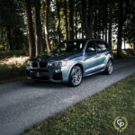 En elegant BMW X3 SUV parkeret på en skyggefuld vej, omgivet af frodige træer, viser sit dynamiske design og sporty holdning.