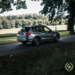 En sølvfarvet BMW X3 parkeret på en fredfyldt, træomkranset vej, der viser sit slanke design og sporty silhuet mod den grønne kulisse af en velholdt græsklædt park under en klar blå himmel