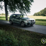 En BMW X3 parkeret på siden af en træklædt vej, udstiller sit sofistikerede design og sporty holdning på baggrund af frodige grønne områder under en klar himmel.