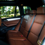 Luksuriøs BMW X3 SUV-interiør med førsteklasses brune lædersæder med elegante syninger, rigelig benplads og moderne sikkerhedsseler, oplyst af naturligt lys fra det åbne soltag.