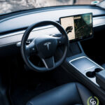 Et elegant interiørbillede af et Tesla Model Y-køretøj, der fremhæver dets minimalistiske design-dashboard, ikoniske rat og store touchscreen-display med navigationskort.