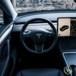 Indvendigt billede af et Tesla Model Y elektrisk køretøj, der viser rattet med firmaets logo og en stor touchskærm på instrumentbrættet.
