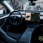 Indvendigt billede af et Tesla Model Y elektrisk køretøj, der viser dets minimalistiske design med en fremtrædende central touchskærm, der viser et kort, og rattet med Tesla-logoet.