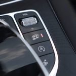 Nærbillede af en Mercedes C43 Cabriolets interiør med start-stop-knap, volumenkontrol og bilstabilitetshjælpeknapper, der viser moderne bildesign med fokus på slanke krom-accenter og taktil