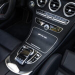 Det luksuriøse interiør i Mercedes C43 Cabriolet fremviser en elegant central kommandokonsol med drejeknapper, krom-accenter og et integreret infotainment-display, alt sammen et eksempel på moderne bilindustriens overdådighed