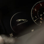 Et nærbillede af en Jaguar F-Pace SUVs instrumentklynge, der fremhæver det ikoniske springende jaguar-logo, med omdrejningsmåleren delvist synlig til højre.