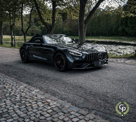 En slank sort Mercedes-Amg Gt C roadster parkeret ved siden af en rolig sø, der emmer af luksus og ydeevne med sin aggressive stil under skumringens bløde skær.