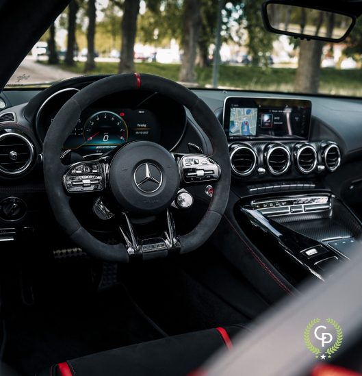 Et luksuriøst bilinteriør med et Mercedes AMG GT C-rat med monterede kontroller, et digitalt instrumentbræt, centralkonsol med infotainmentsystem og førsteklasses finish.