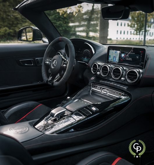 Luksuriøst Mercedes AMG GT C interiør med et moderne instrumentbræt med touchscreen infotainmentsystem, lædersæder med røde syninger og en slank midterkonsol med metalliske accenter, der viser sofistikeret design og avanceret teknologi