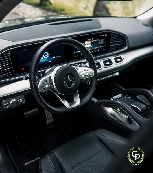 Indvendig visning af en Mercedes GLE350de, der viser et moderne instrumentbræt med digitale displays, rat med betjeningsknapper og luksuriøse finish.