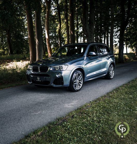 En elegant BMW X3 SUV parkeret på en skyggefuld vej, omgivet af frodige træer, viser sit dynamiske design og sporty holdning.