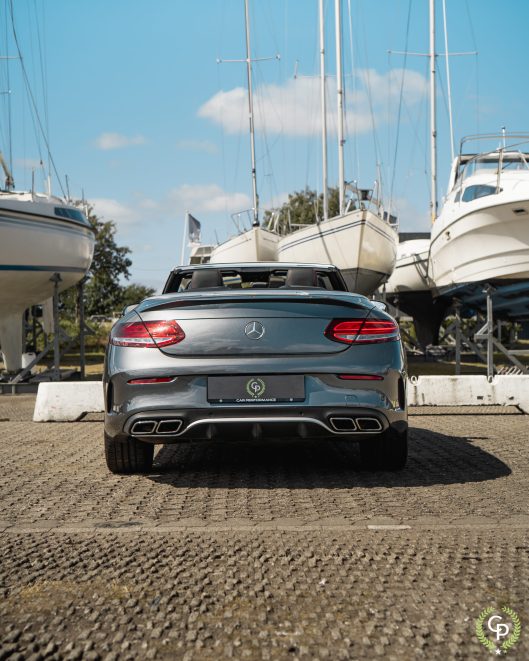 En sølvfarvet Mercedes C43 Cabriolet parkeret ved en lystbådehavn, med dets luksuriøse design sidestillet med en række forankrede sejlbåde under en klar blå himmel.